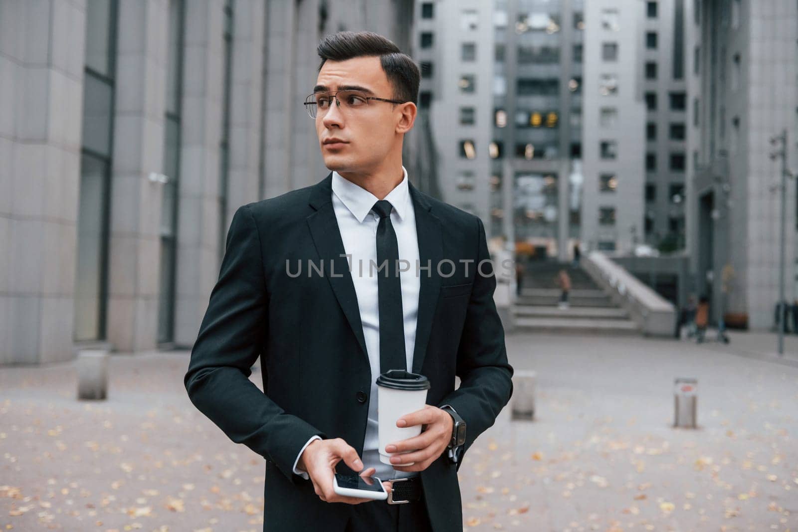 Busy man. Businessman in black suit and tie is outdoors in the city.