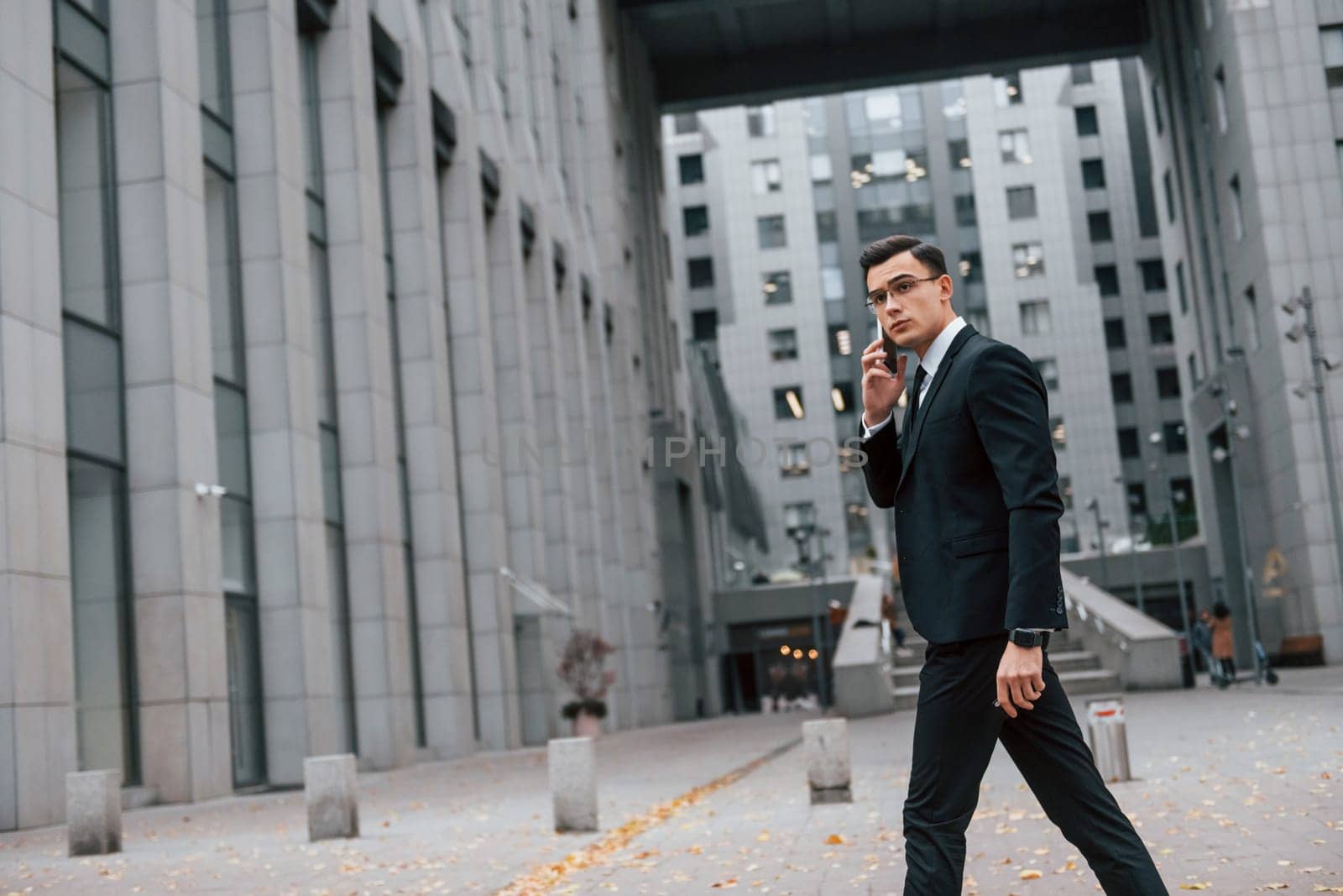 Busy man. Businessman in black suit and tie is outdoors in the city.