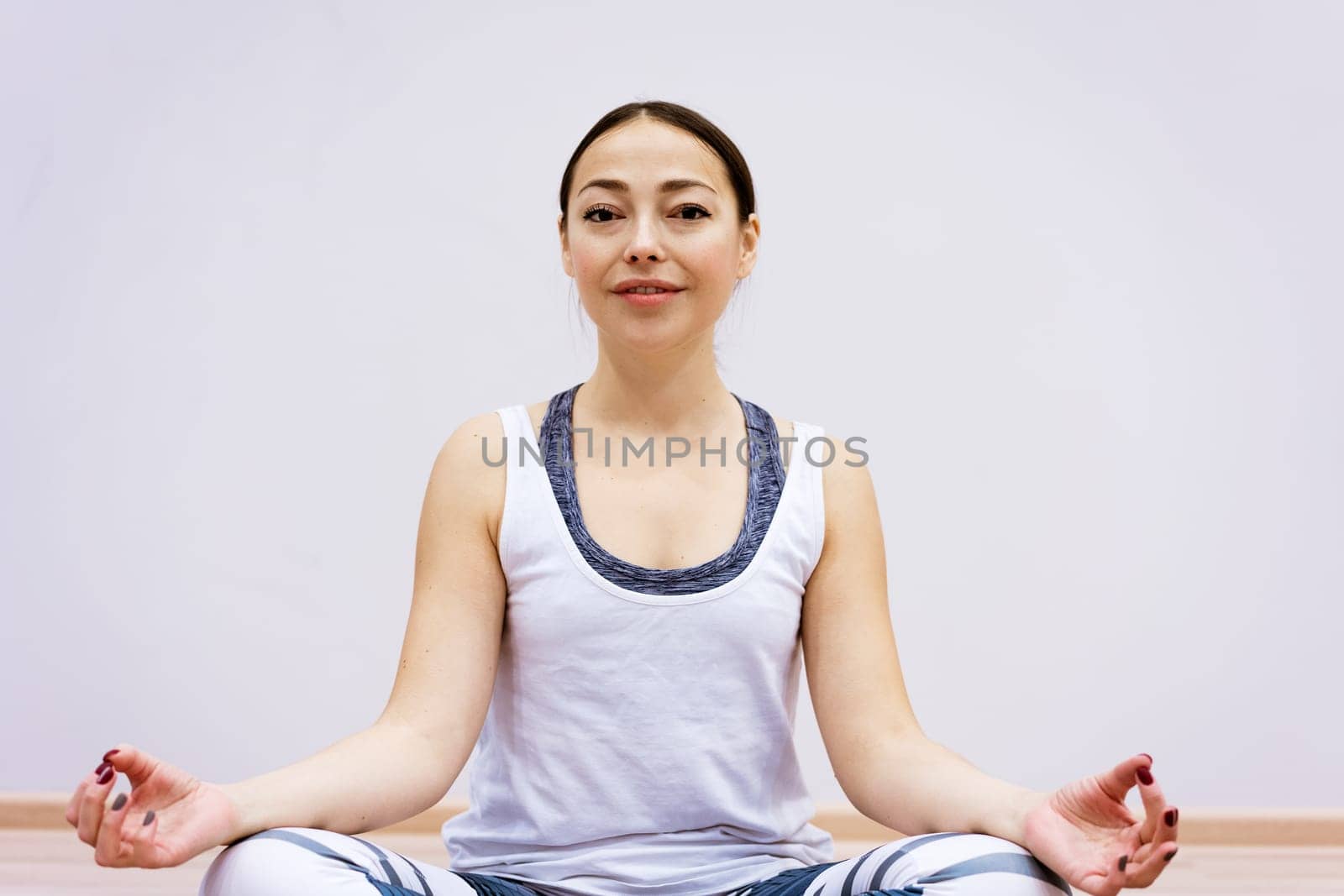 Happy caucasian woman in sportswear practices yoga at home against a wall background. The concept of a healthy lifestyle and inner spirit. Body concentration