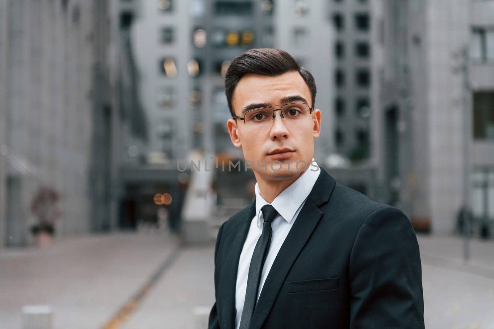 Portrait of businessman that is in black suit and tie is outdoors in the city.