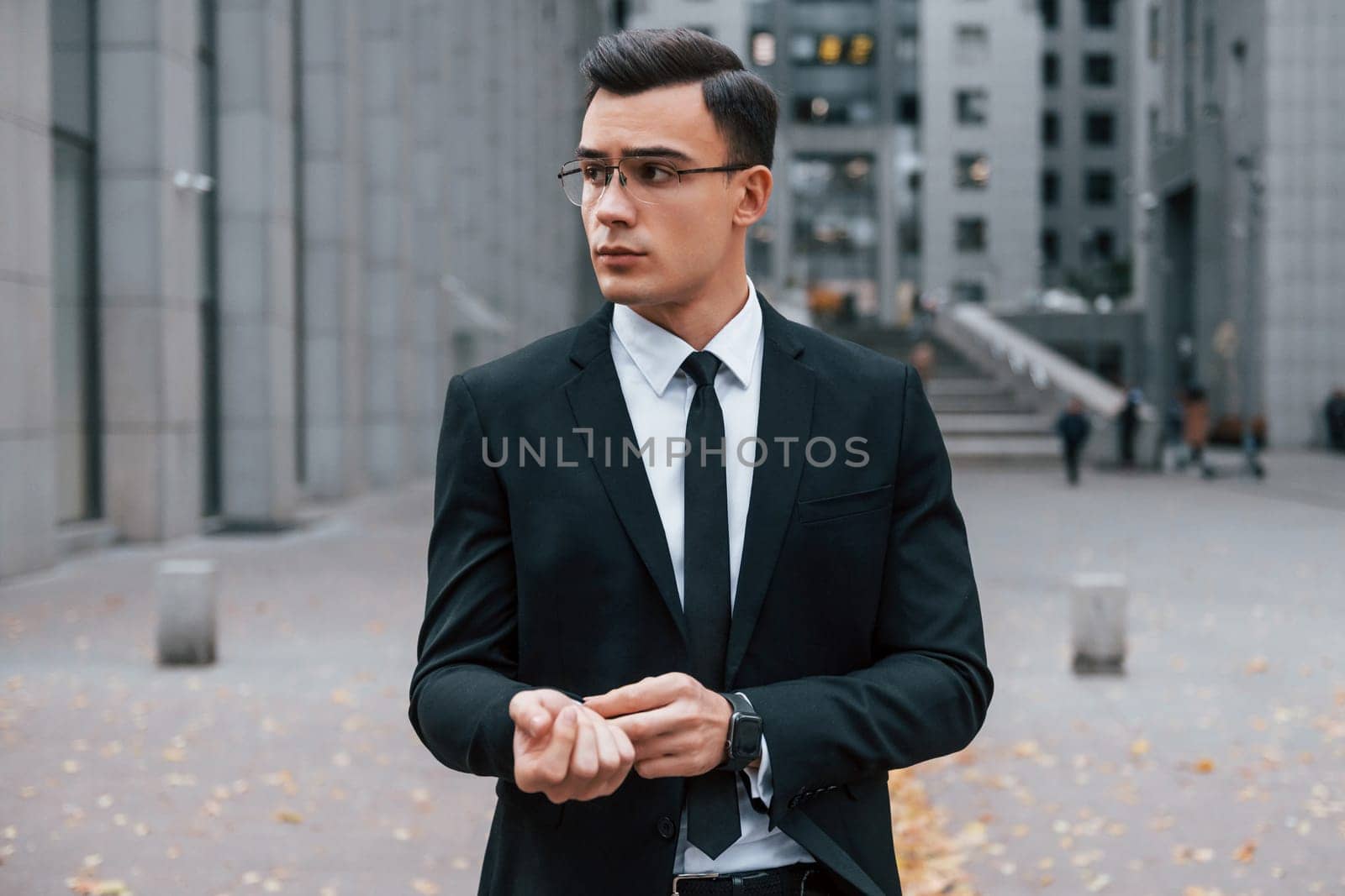 Portrait of businessman that is in black suit and tie is outdoors in the city.