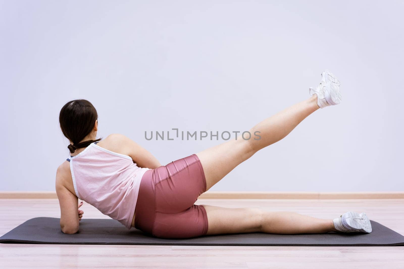 A woman of Caucasian ethnicity in sportswear is engaged in fitness at home against the background of a wall. Healthy lifestyle and slim body concept