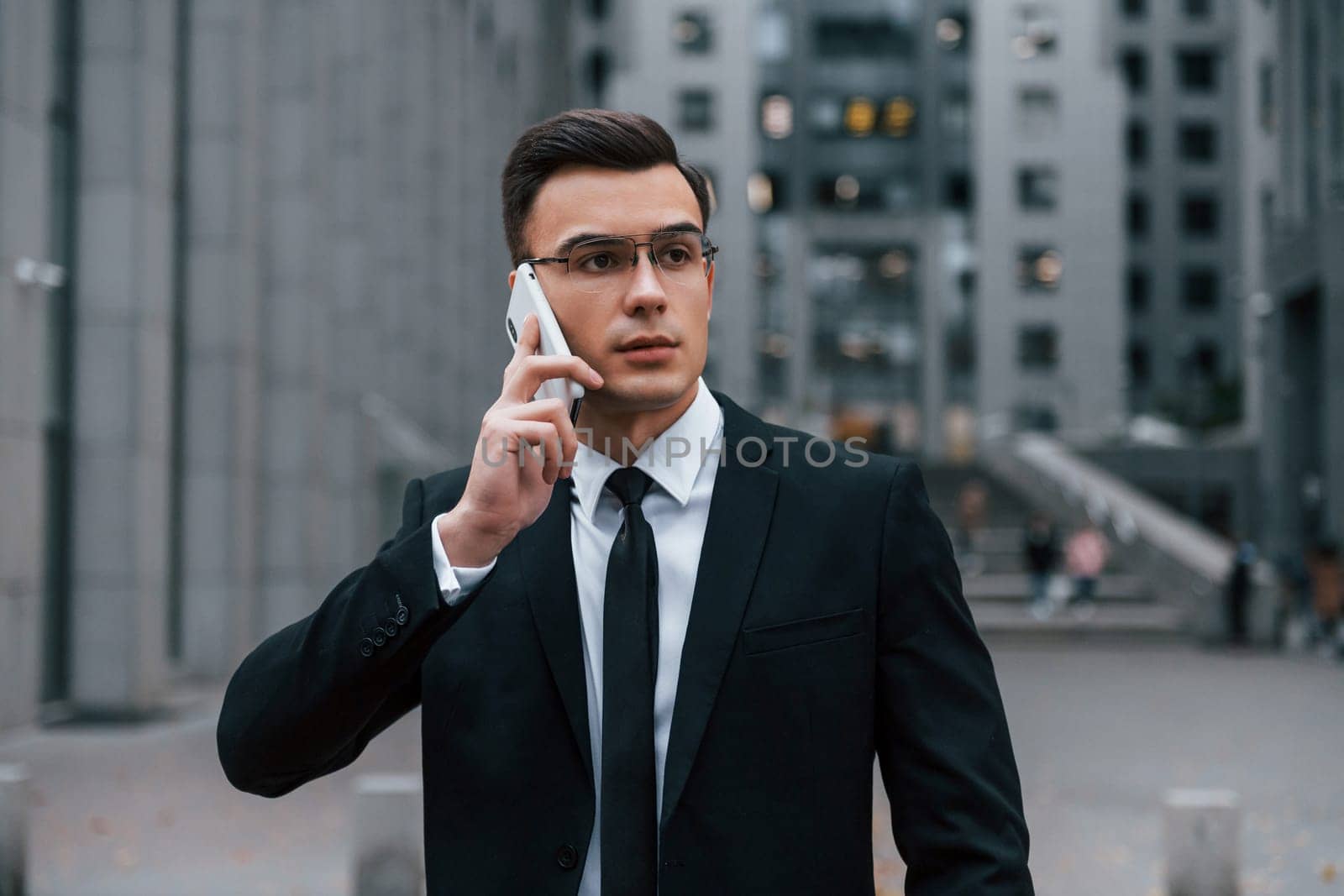 Portrait of businessman that is in black suit and tie is outdoors in the city.