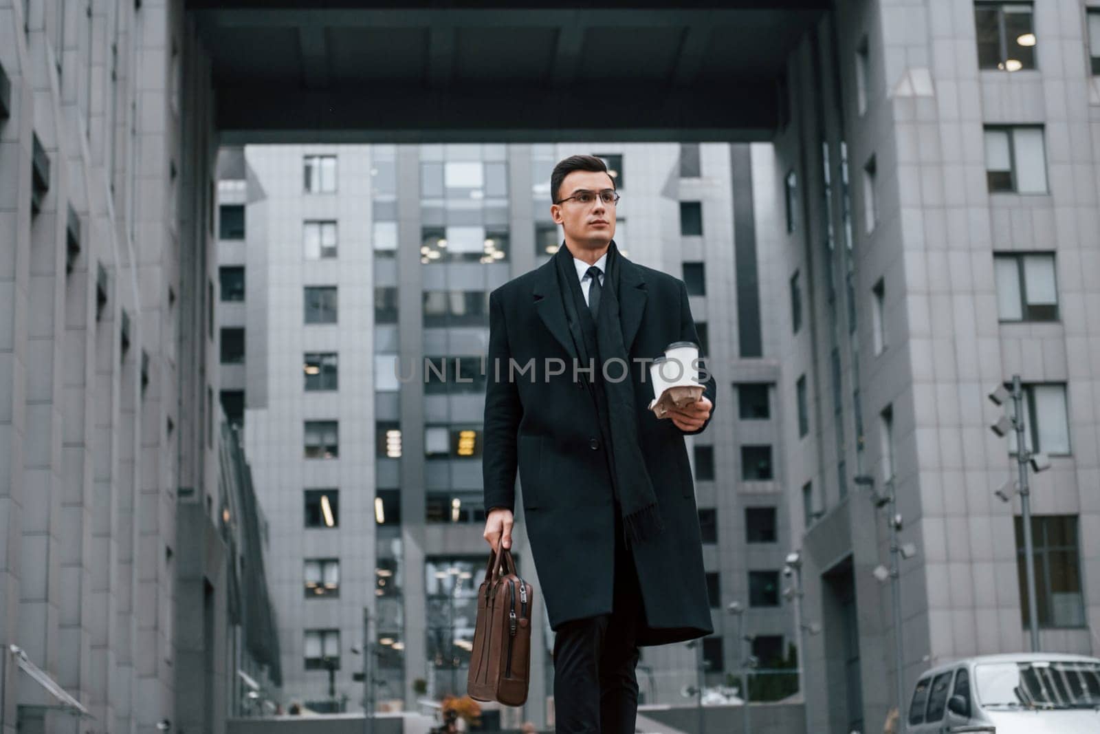 Fresh drink. Businessman in black suit and tie is outdoors in the city.