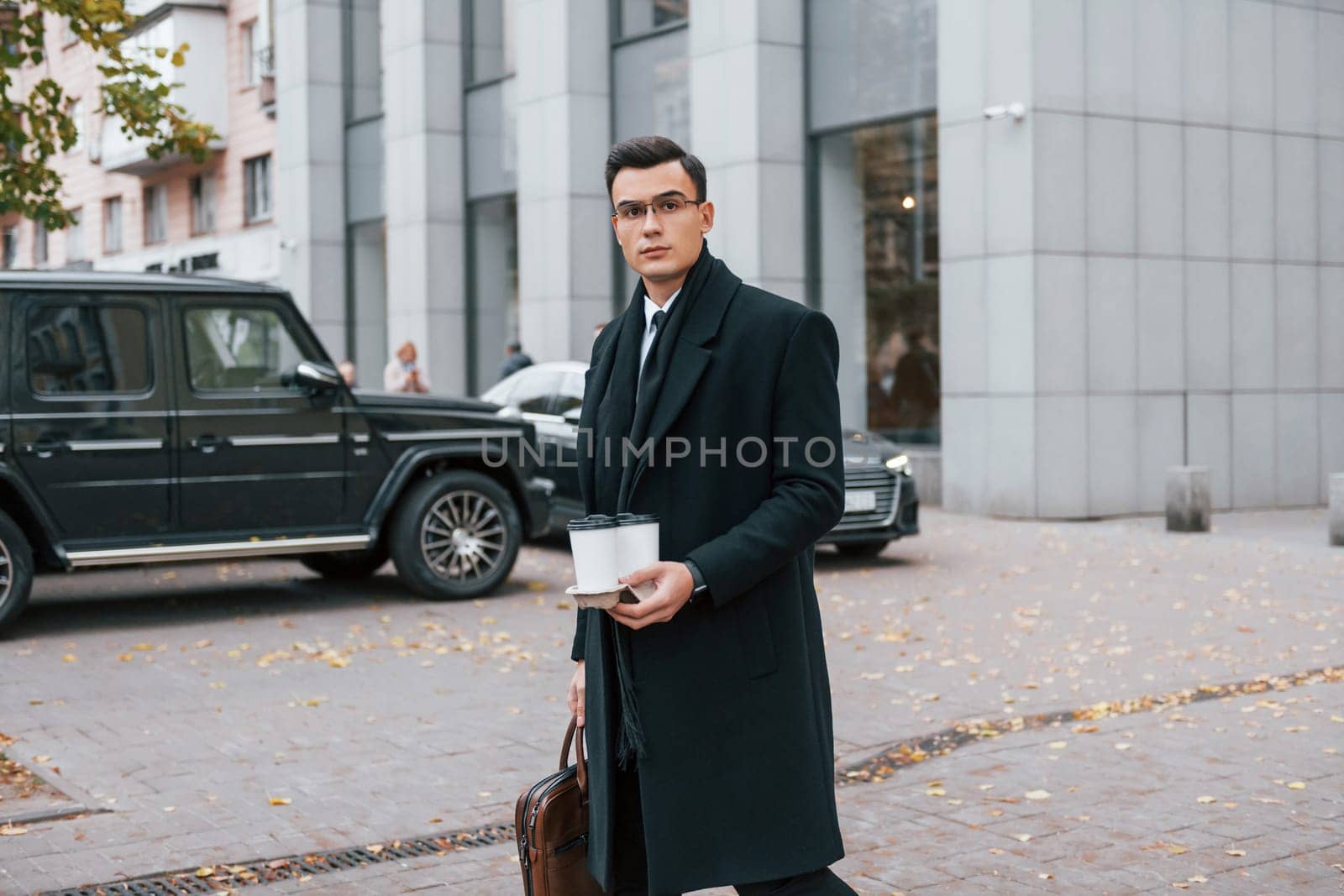 Fresh drink. Businessman in black suit and tie is outdoors in the city by Standret