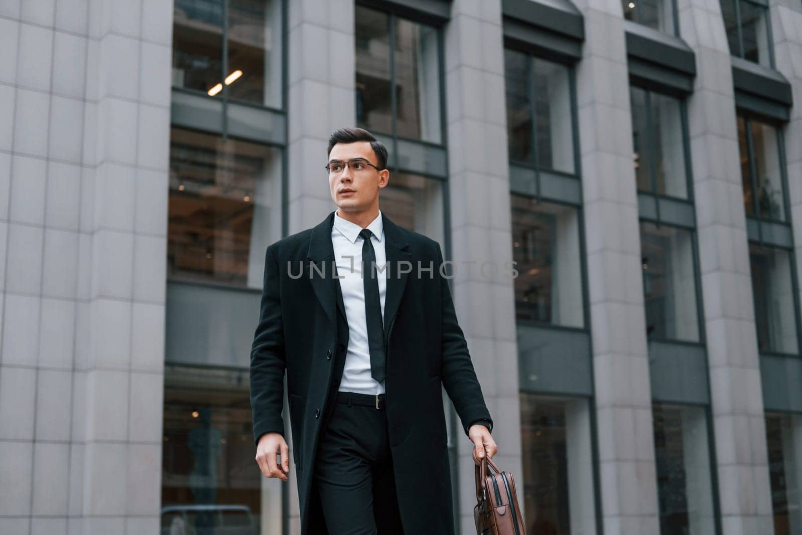 Conception of formal clothes. Businessman in black suit and tie is outdoors in the city.