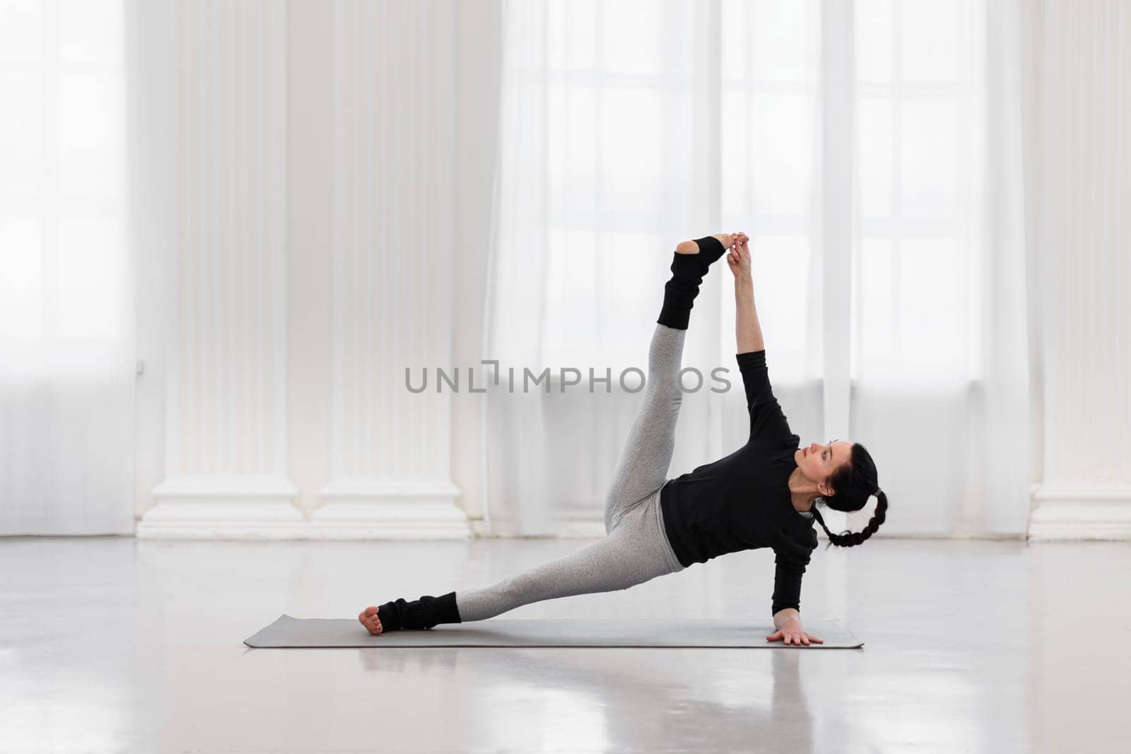 Charming young woman doing vertical splits during yoga class in a cozy gym. The concept of flexibility, leg and back muscle tone, balance and concentration by apavlin