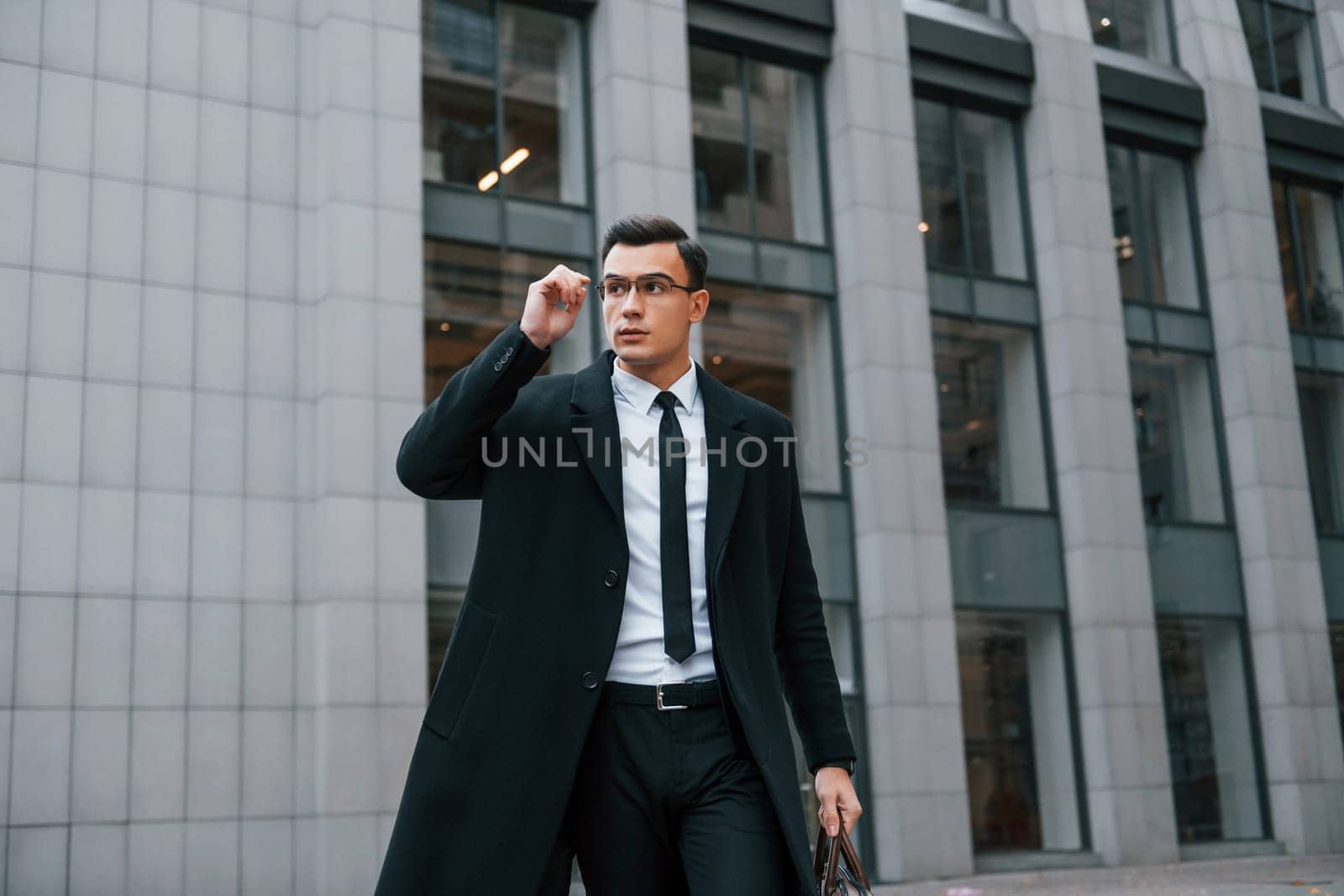 Conception of formal clothes. Businessman in black suit and tie is outdoors in the city.