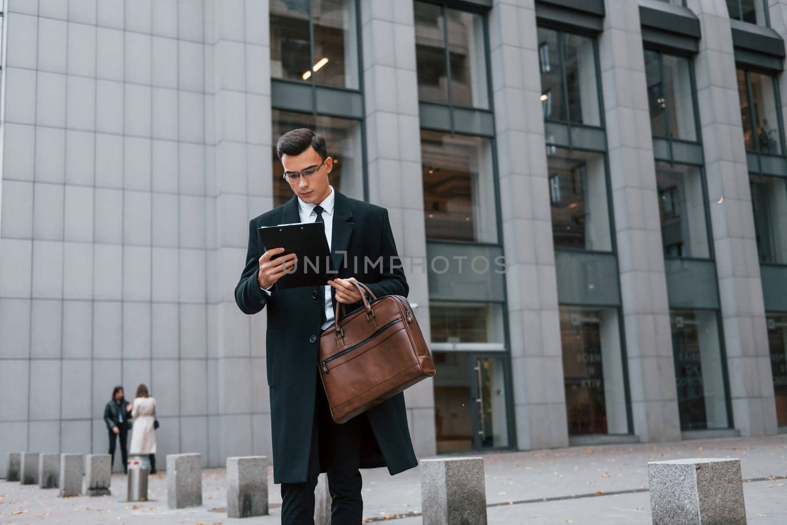 Conception of formal clothes. Businessman in black suit and tie is outdoors in the city by Standret