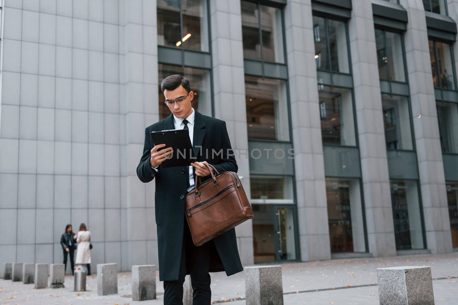 Conception of formal clothes. Businessman in black suit and tie is outdoors in the city.