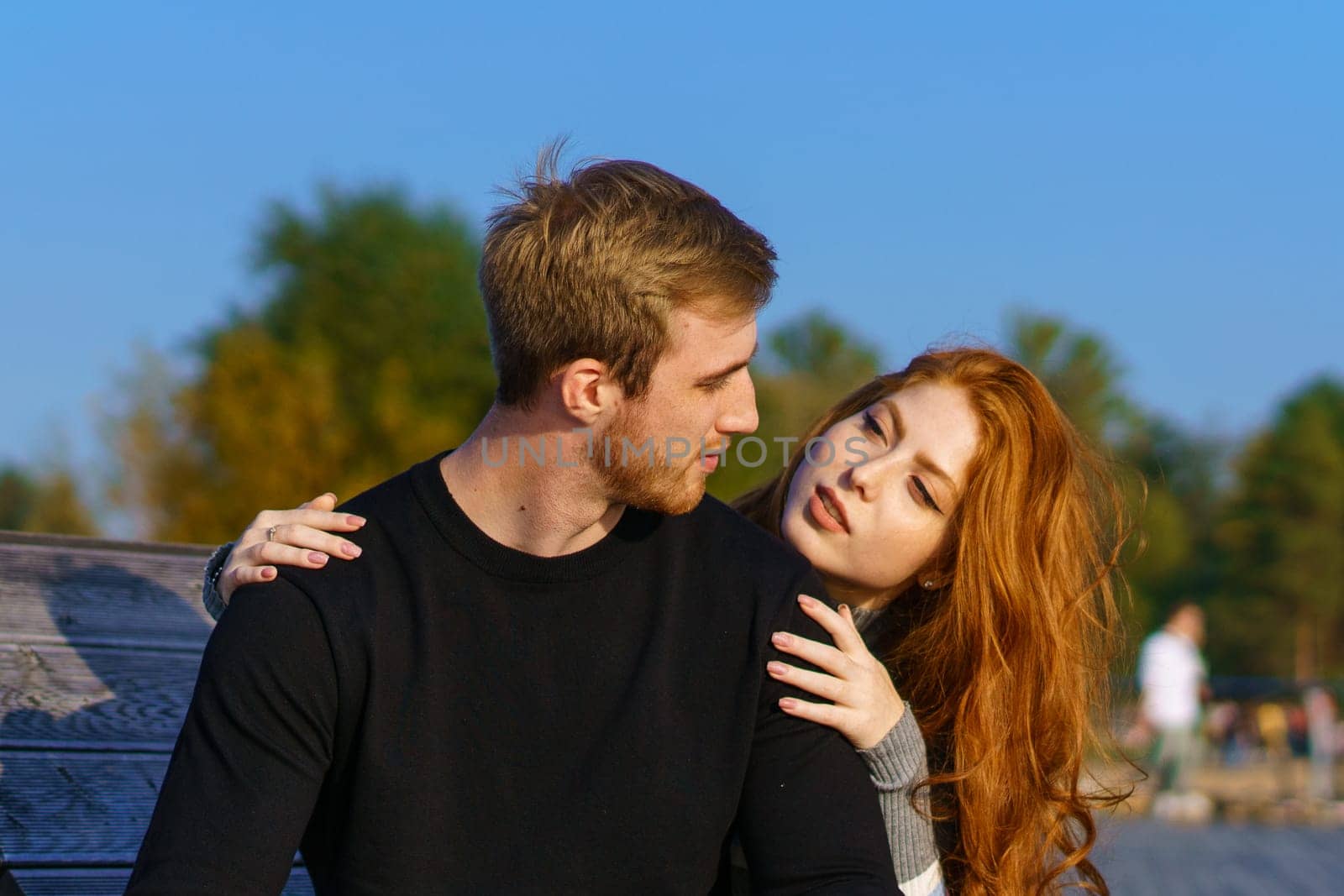 young couple are sitting in the park on a wooden bench hugging by EkaterinaPereslavtseva