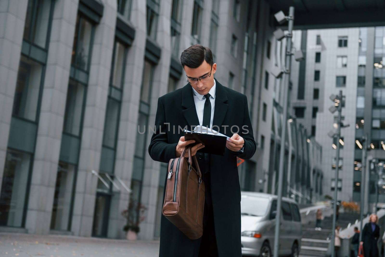 With notepad in hands. Businessman in black suit and tie is outdoors in the city.