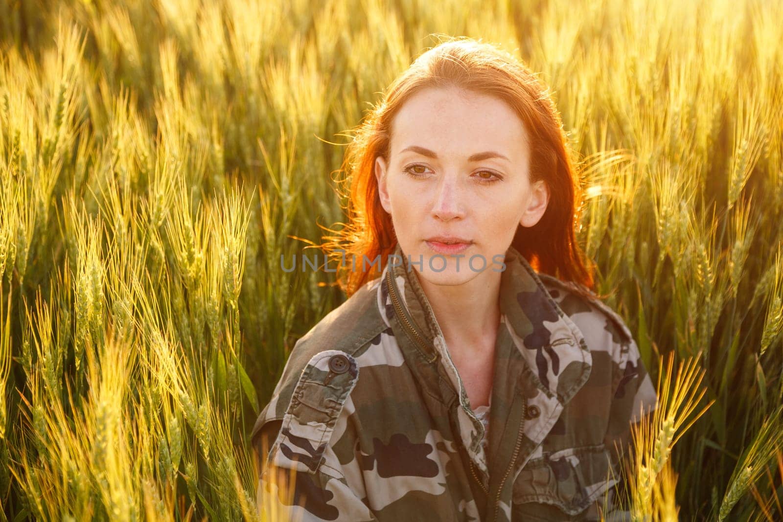 Portrait of a young happy girl sitting on a golden wheat harvest in a yellow sunset field. summer nature background. woman with red hair. young woman sitting in a wheat field