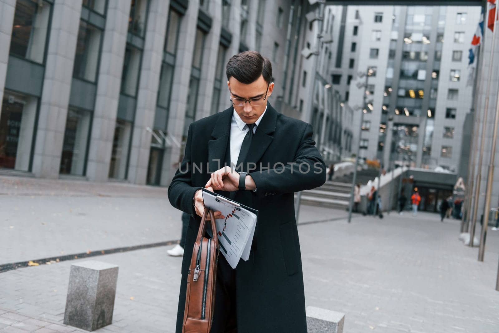 Busy for a work. Businessman in black suit and tie is outdoors in the city by Standret