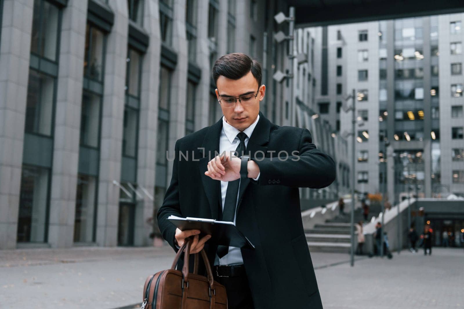 With notepad in hands. Businessman in black suit and tie is outdoors in the city.