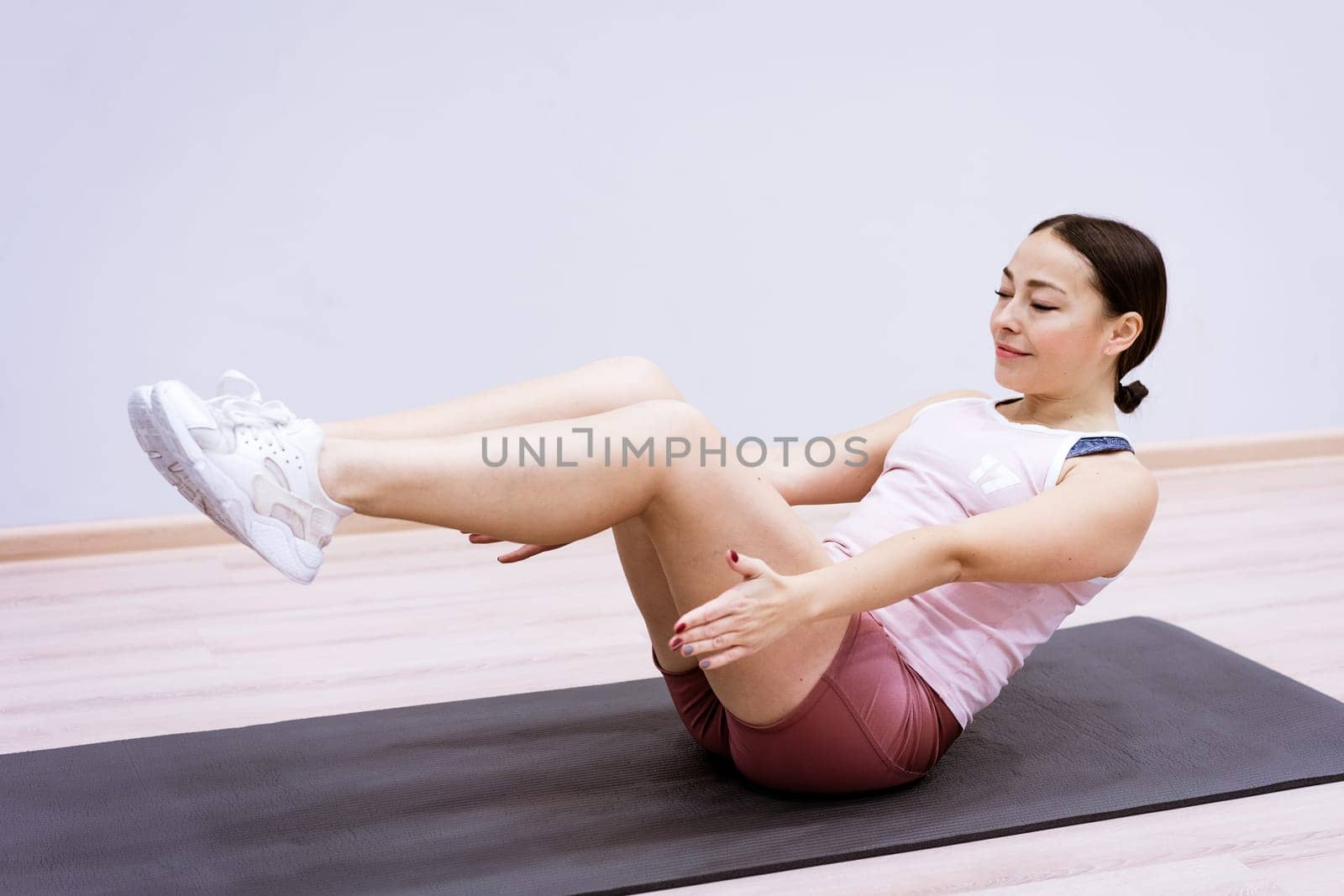 A woman of Caucasian ethnicity in sportswear is engaged in fitness at home against the background of a wall. Healthy lifestyle and slim body concept