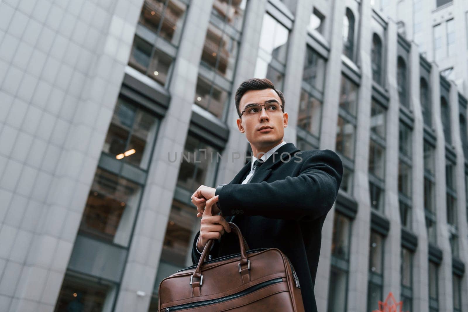 Checking the time. Businessman in black suit and tie is outdoors in the city by Standret