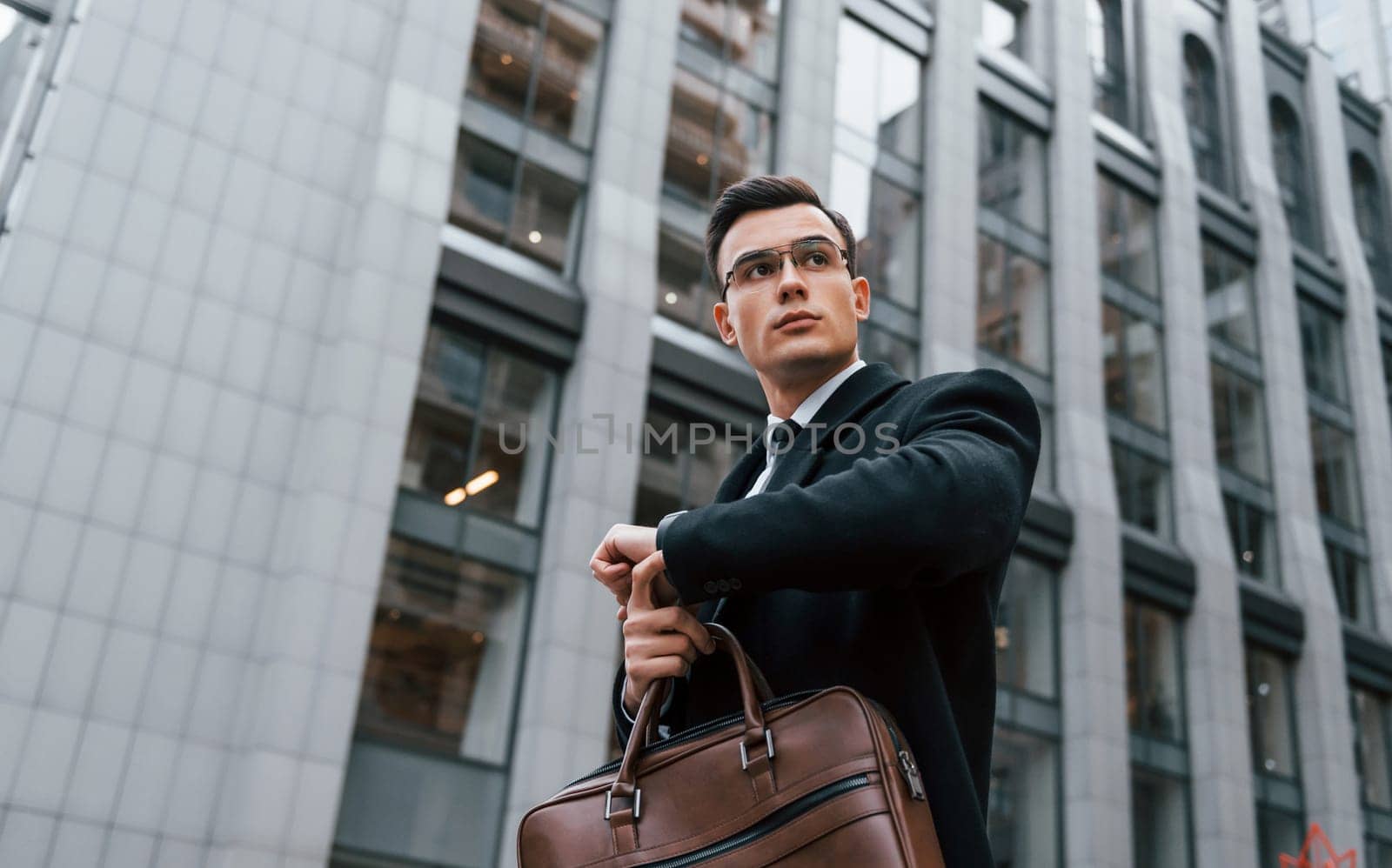 Checking the time. Businessman in black suit and tie is outdoors in the city.