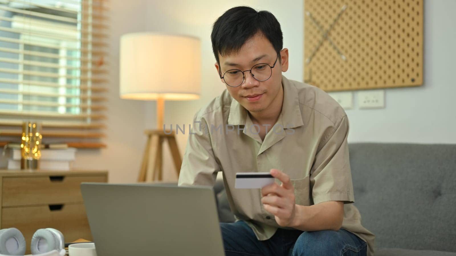 Pleasant man holding credit card and using laptop making transaction on internet banking. Online shopping, e-commerce.