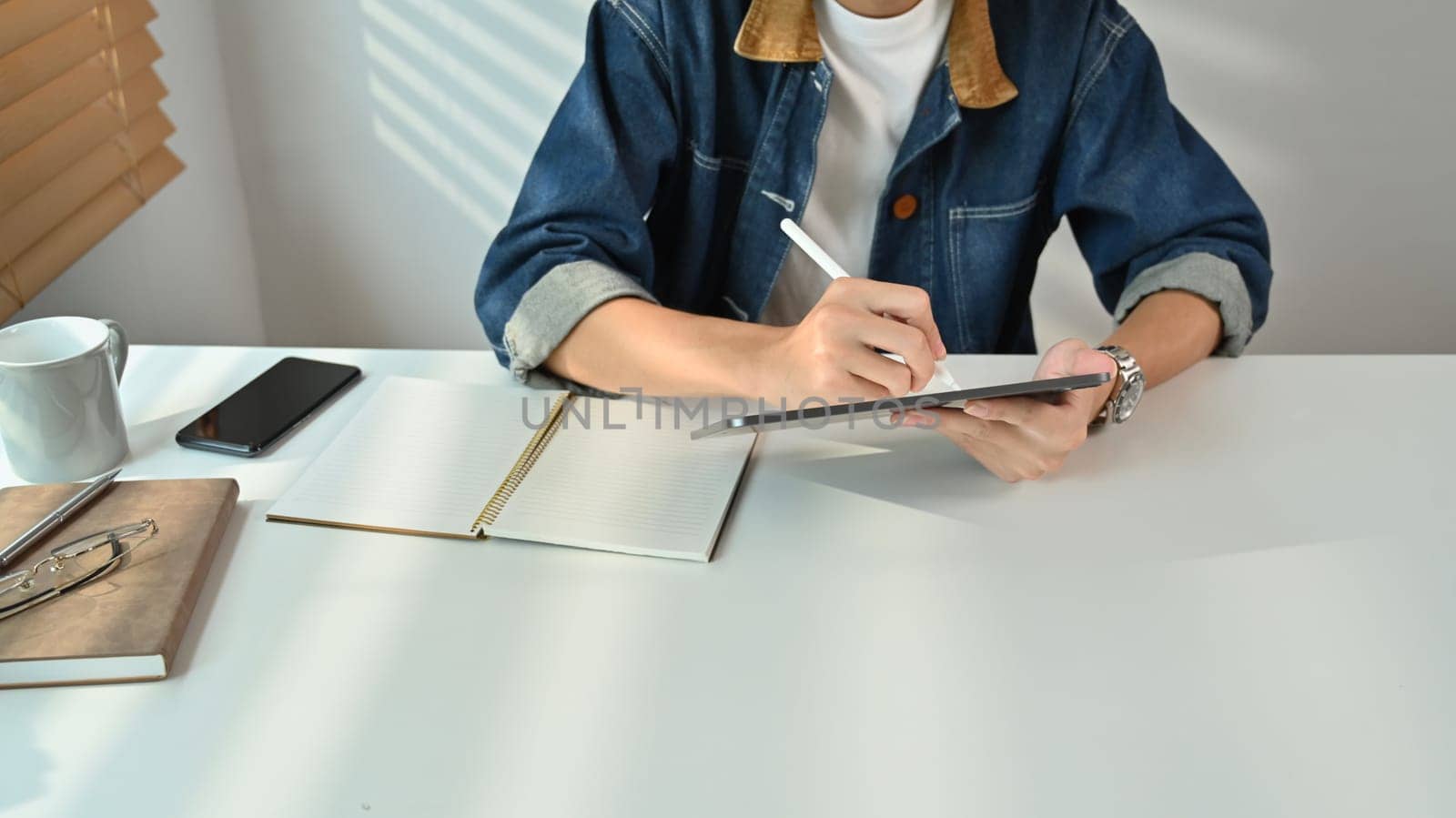 Man freelancer wearing jeans jacket browsing internet or sending email on digital tablet during working at home.