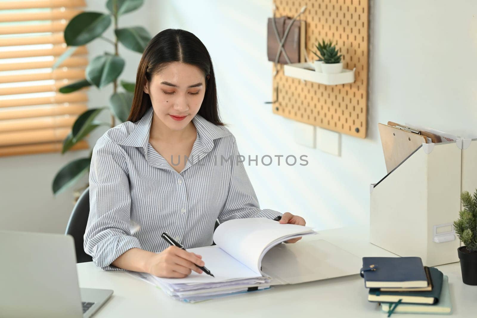 Concentrated female worker analyzing sales statistics document, signing contracts at her working desk.