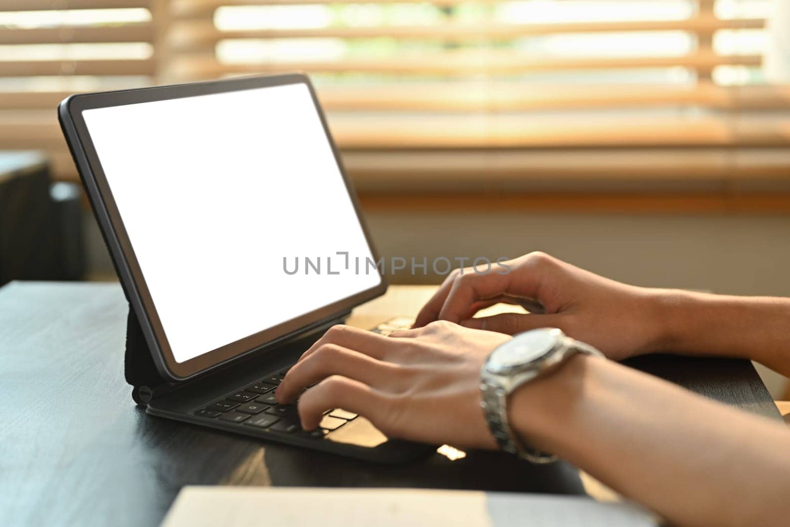 Close up view of man typing on keyboard of digital tablet, communicating online, distantly working or studying on computer at home by prathanchorruangsak