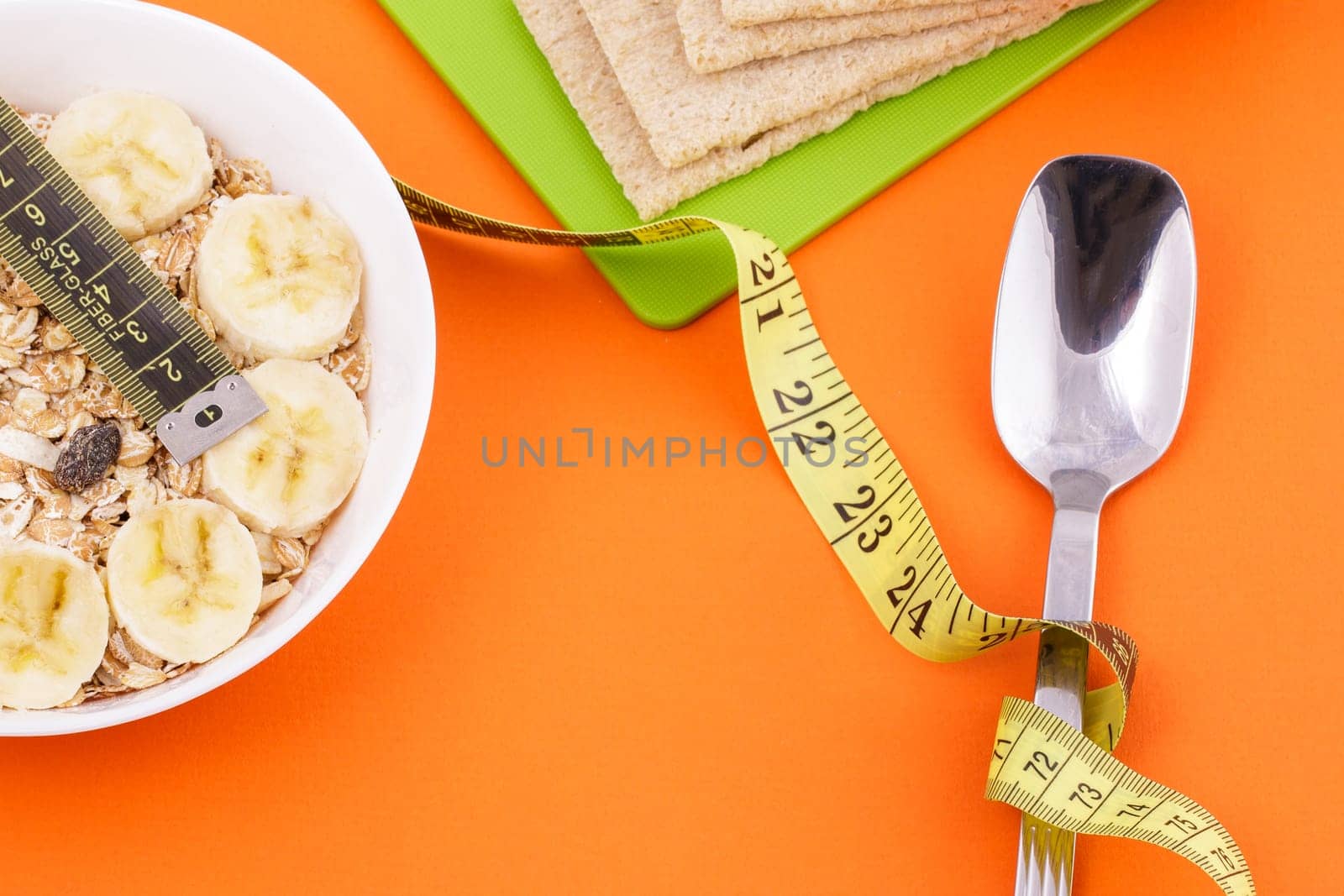 oatmeal and crispbread lie with spoon and measuring tape on orange background by EkaterinaPereslavtseva