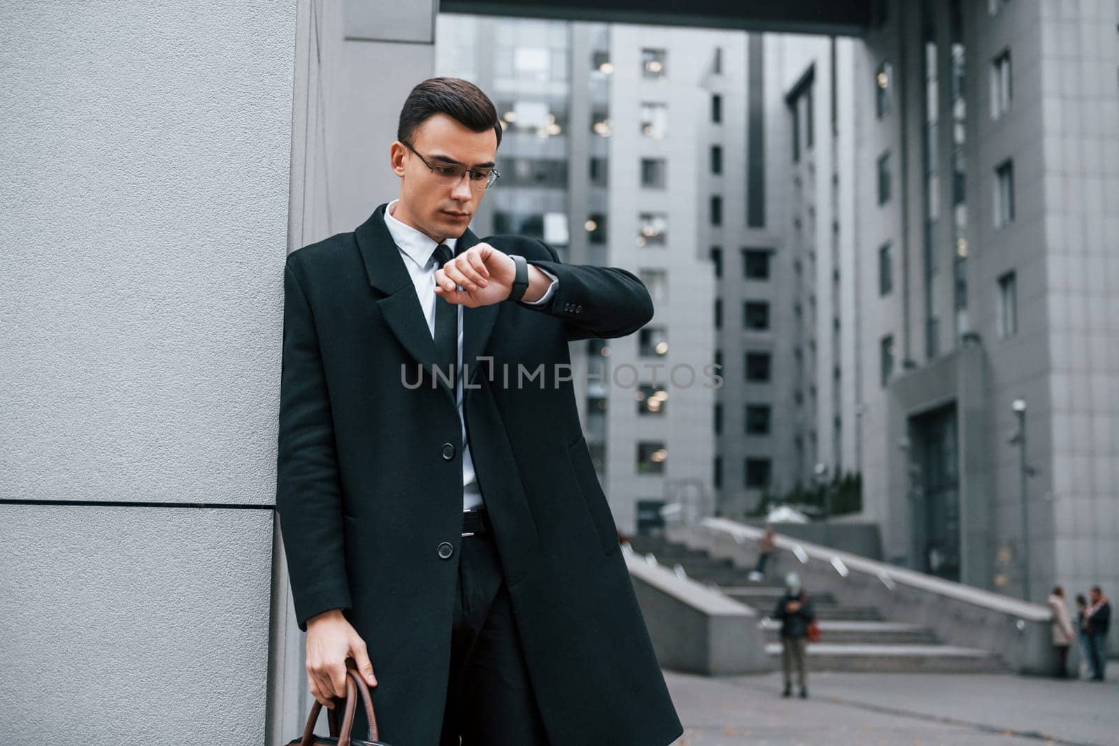 Standing near the building. Businessman in black suit and tie is outdoors in the city.
