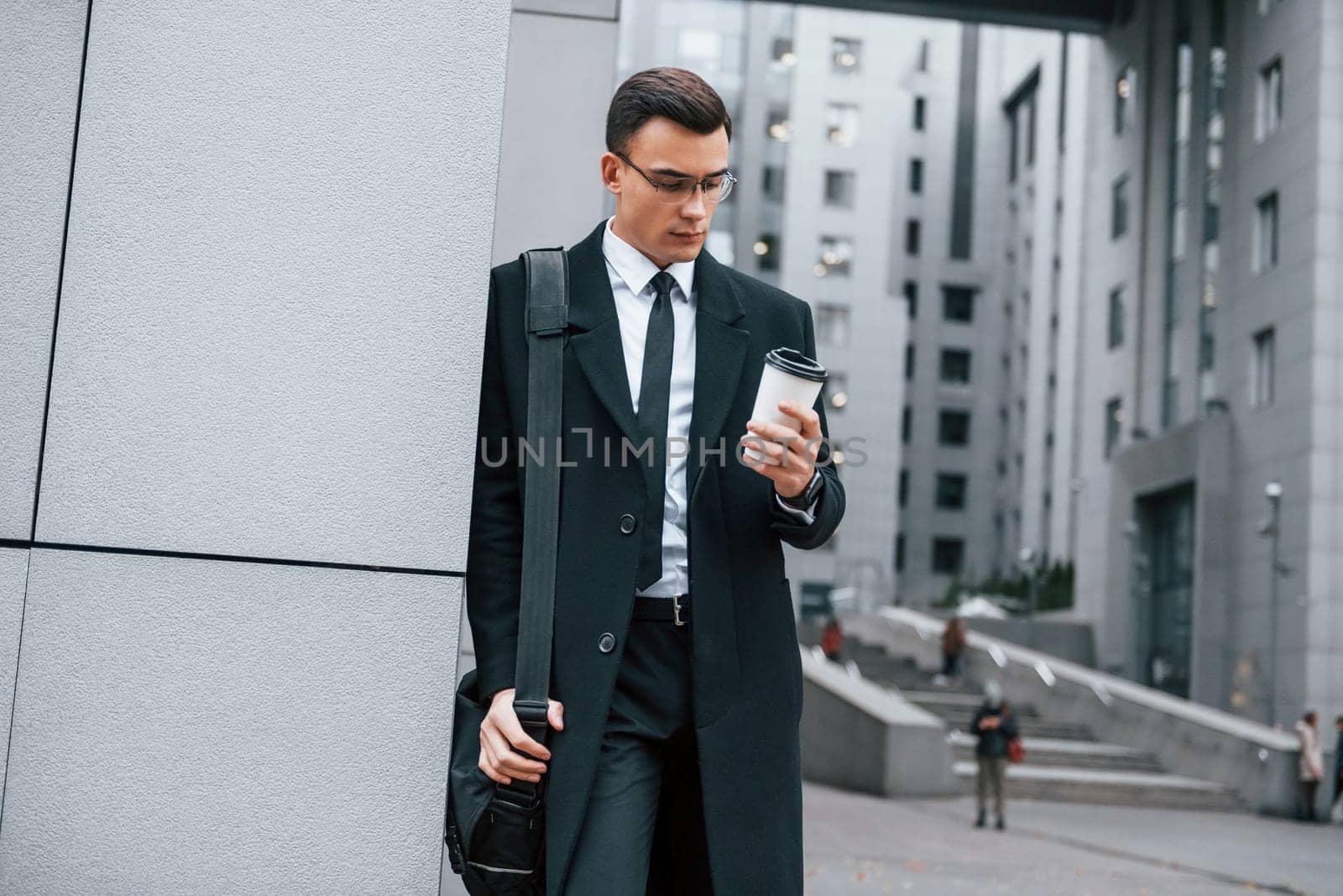 Standing near the building. Businessman in black suit and tie is outdoors in the city.