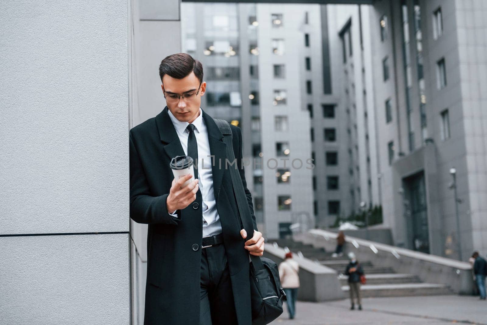 Standing near the building. Businessman in black suit and tie is outdoors in the city.