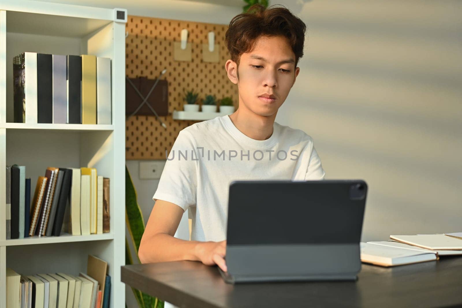 Young asian male looking at digital tablet, working or doing research or preparing for exam online. Education and technology.
