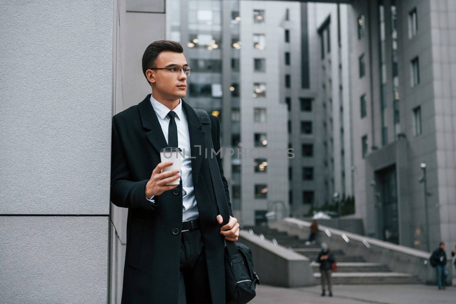 Standing near the building. Businessman in black suit and tie is outdoors in the city.