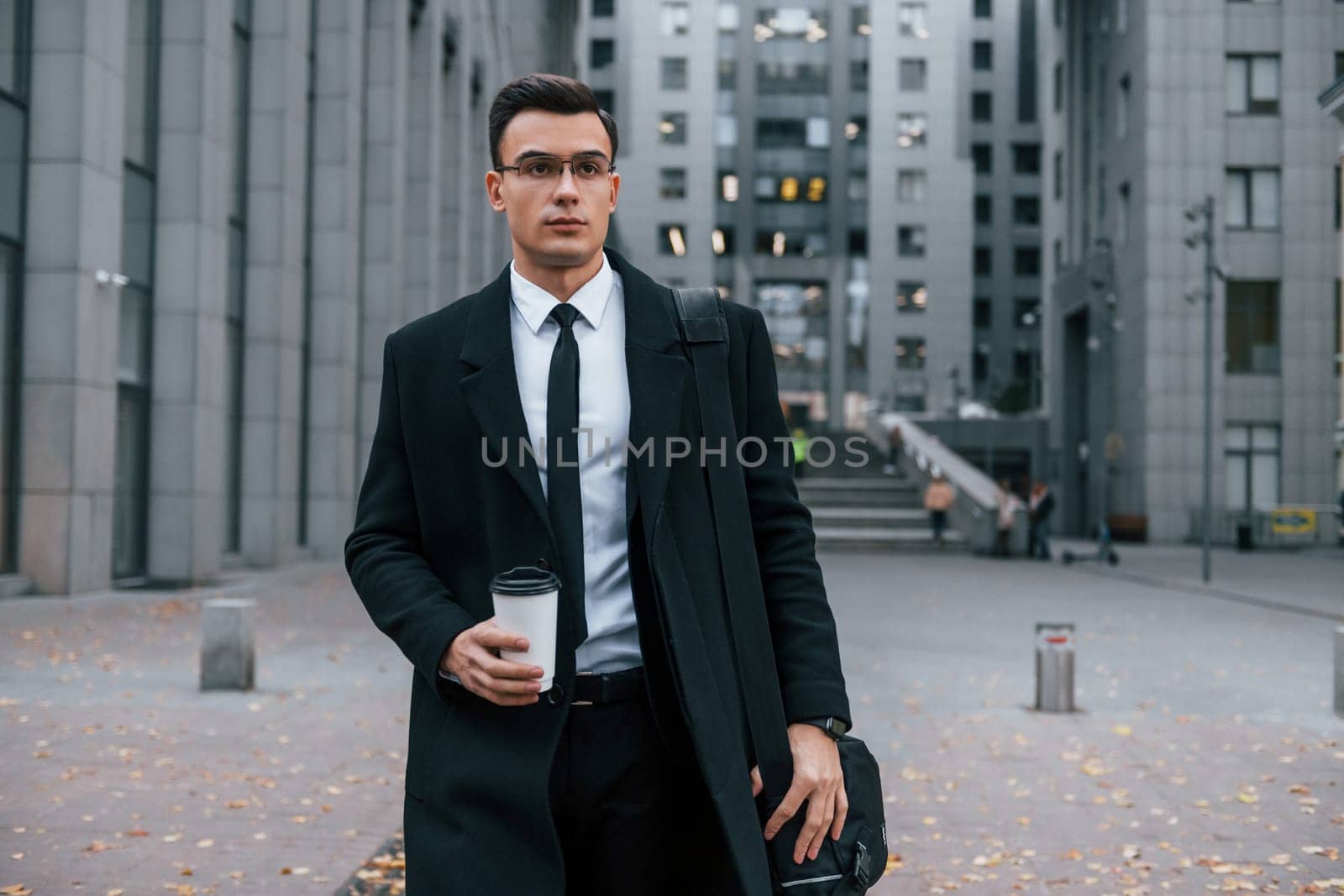 Businessman in black suit and tie is outdoors in the city by Standret