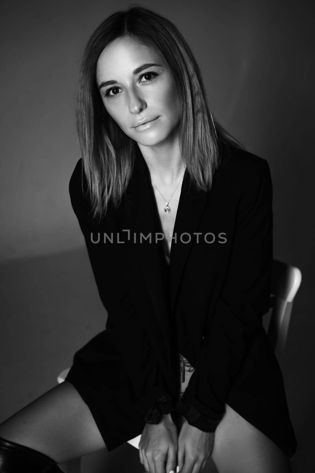 beautiful woman of Caucasian ethnicity posing sitting on a chair in a black jacket and lingerie, black and white photo. Dark photo of seductive sexy girl