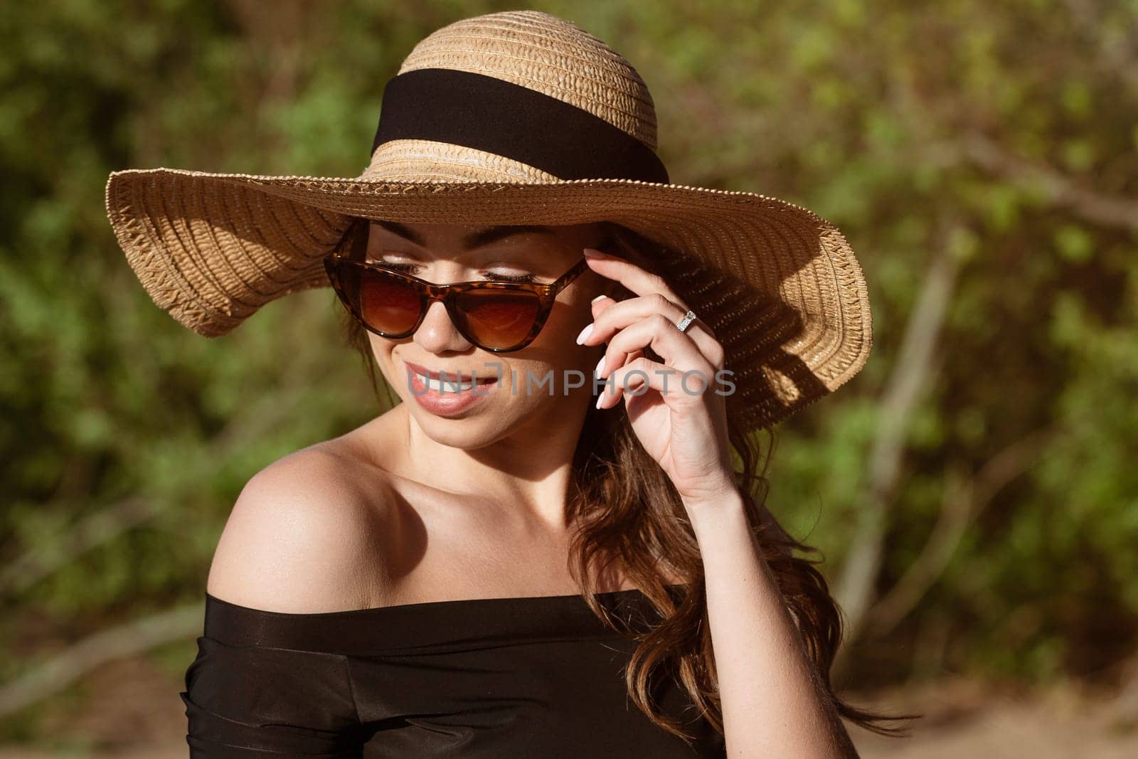 Young happy woman of Caucasian appearance in a straw hat close-up in sunglasses posing on a sunny summer day on the beach.