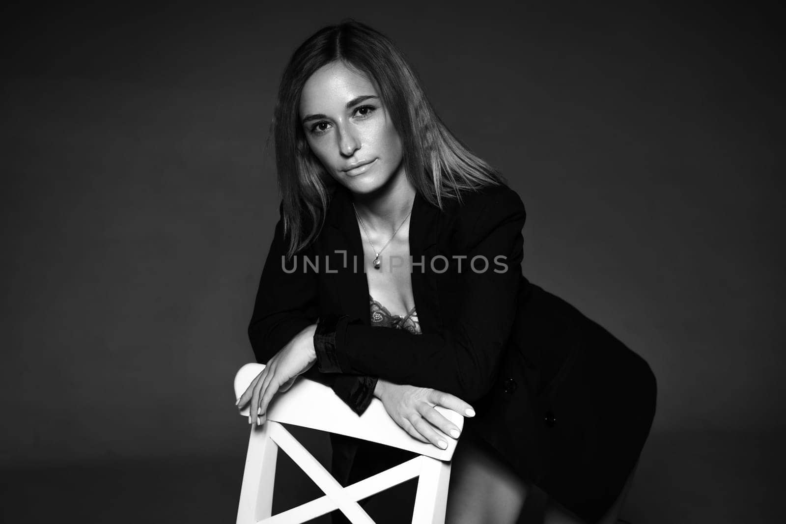 beautiful woman of Caucasian ethnicity posing sitting on a chair in a black jacket and lingerie, black and white photo. Dark photo of seductive sexy girl