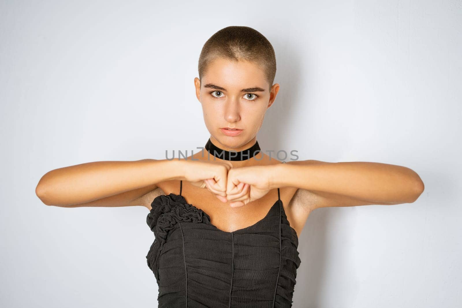 Portrait of a young woman with a short haircut in a black dress with clenched fists on a light background