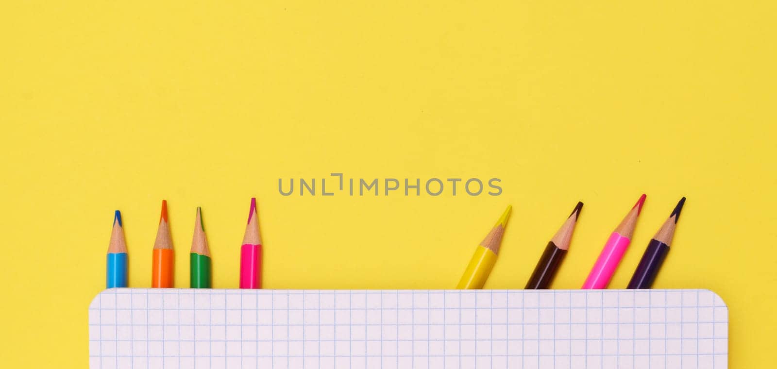 Colorful stationery is placed under a notebook on a yellow background, top view, for advertising.