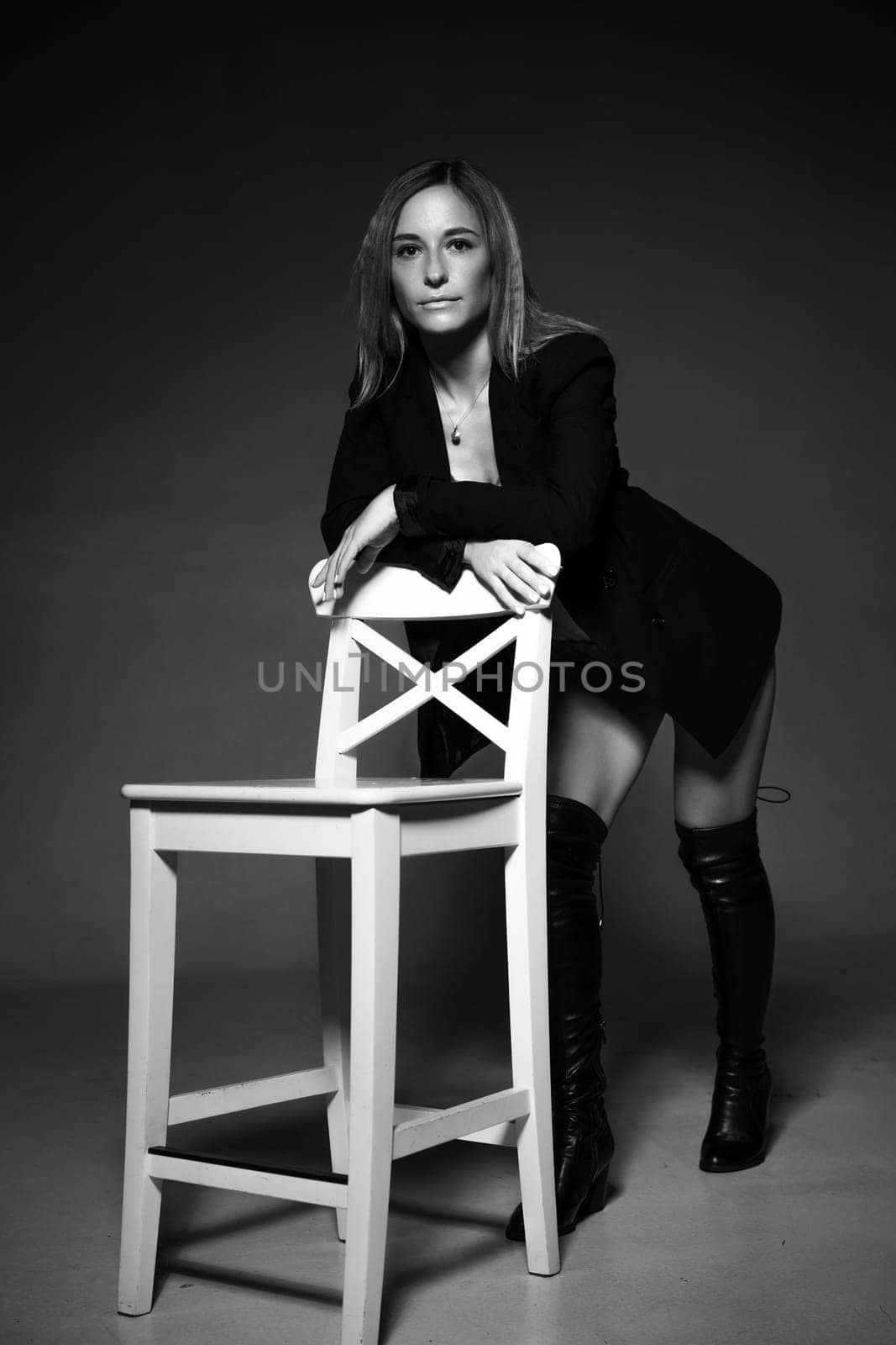 beautiful woman of Caucasian ethnicity posing sitting on a chair in a black jacket and lingerie, black and white photo. Dark photo of seductive sexy girl