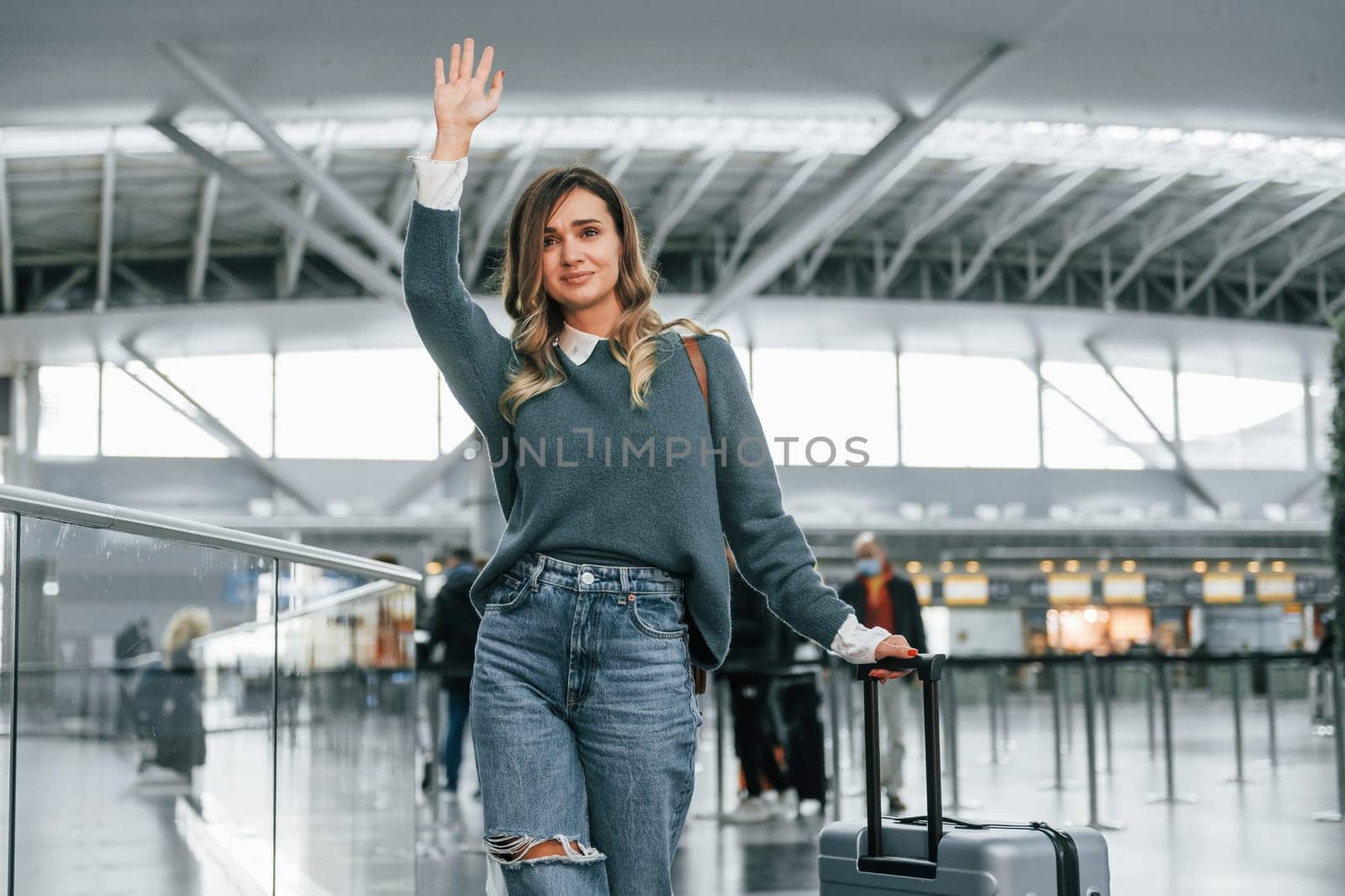 Hello gesture. Young female tourist is in the airport at daytime.