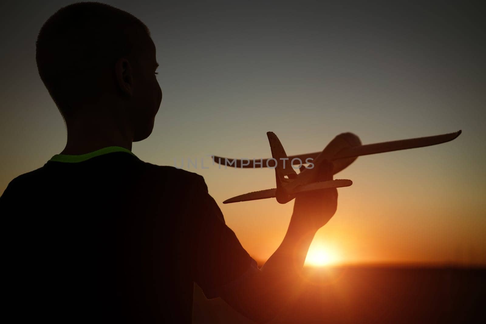 Boy throws a toy airplane in the summer at sunset. A child plays with a toy airplane, dreams of a trip. Son plays by plane in the field at sunset. Have fun and enjoy life