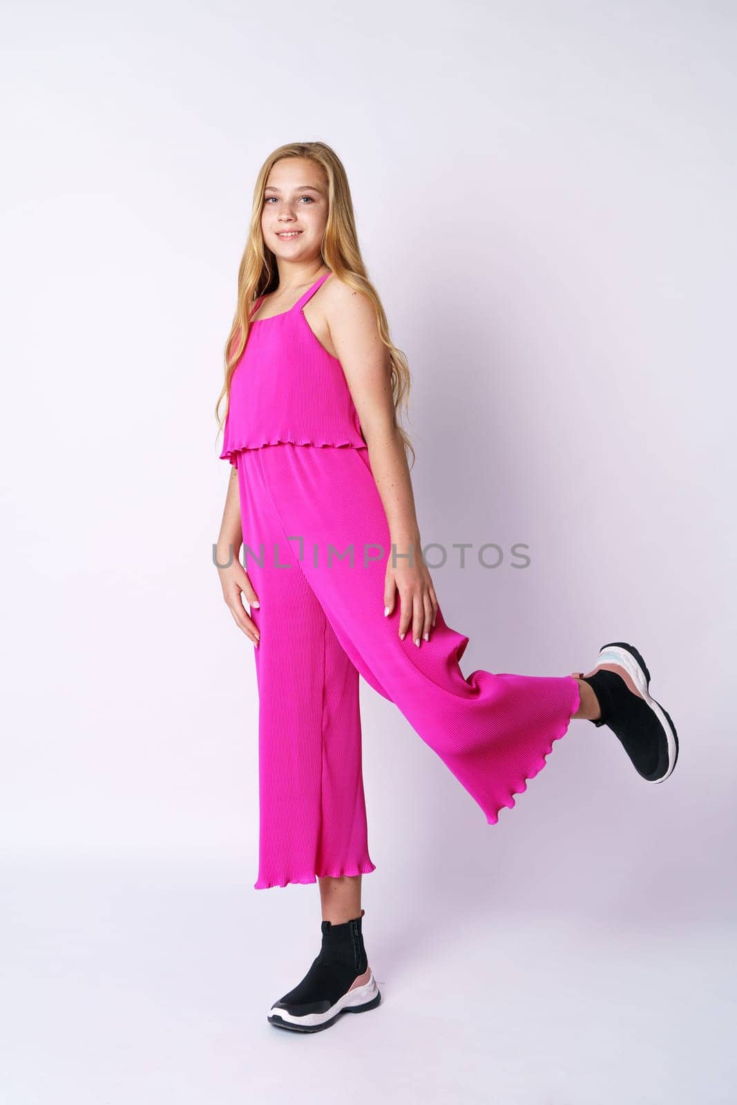 Beautiful girl teenager posing in a pink jumpsuit on a white background. Stylish and youthful bright clothes for a young professional fashion model