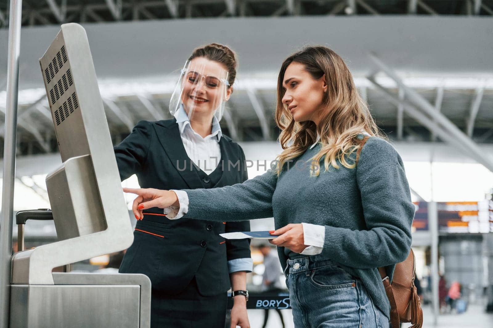 Employee helping to use terminal. Young female tourist is in the airport at daytime by Standret