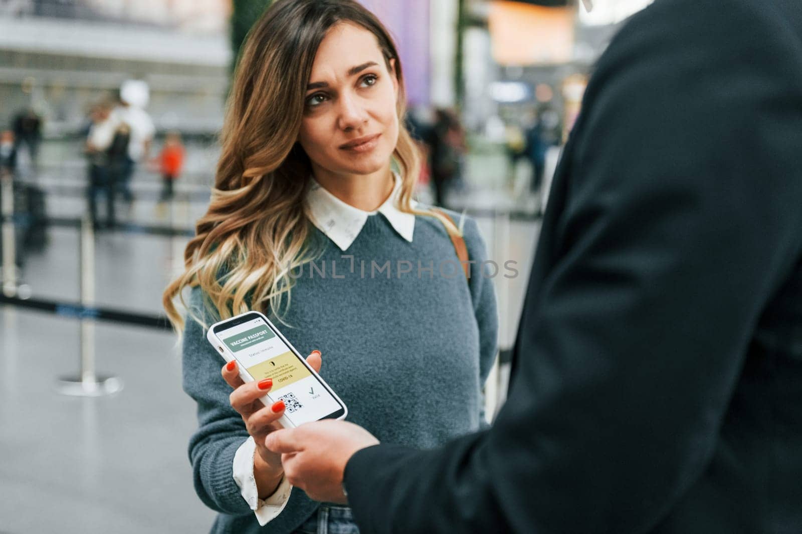 Certificate of vaccination in the phone. Young female tourist is in the airport at daytime.