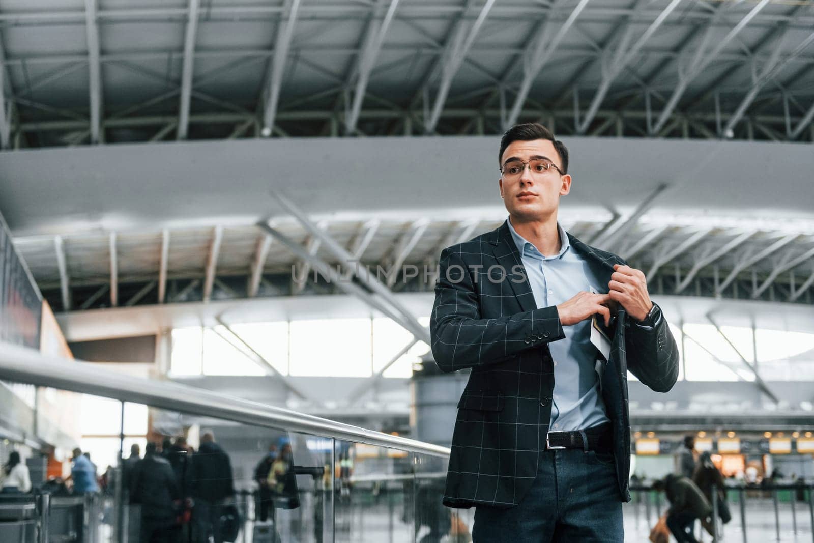 Taking out the documents. Young businessman in formal clothes is in the airport at daytime.