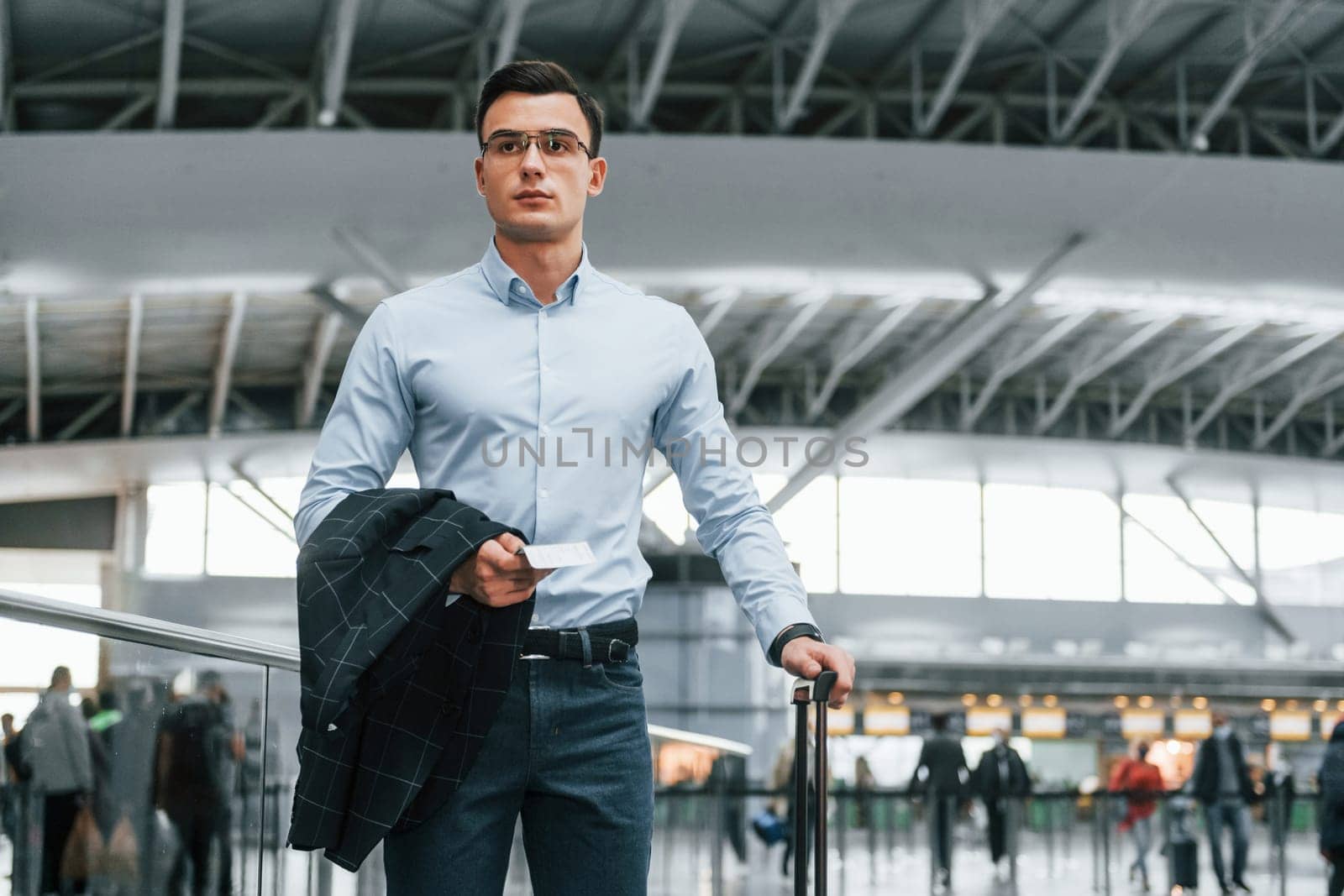 Front view. Young businessman in formal clothes is in the airport at daytime.
