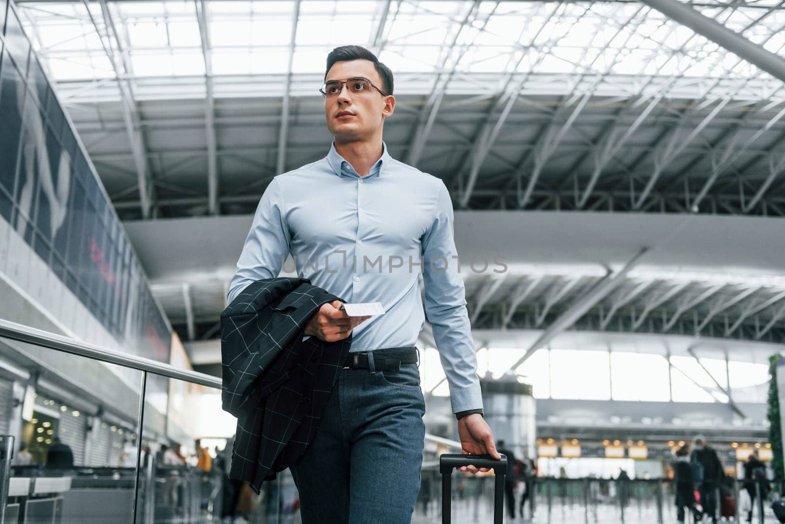 Holding jacket. Young businessman in formal clothes is in the airport at daytime.