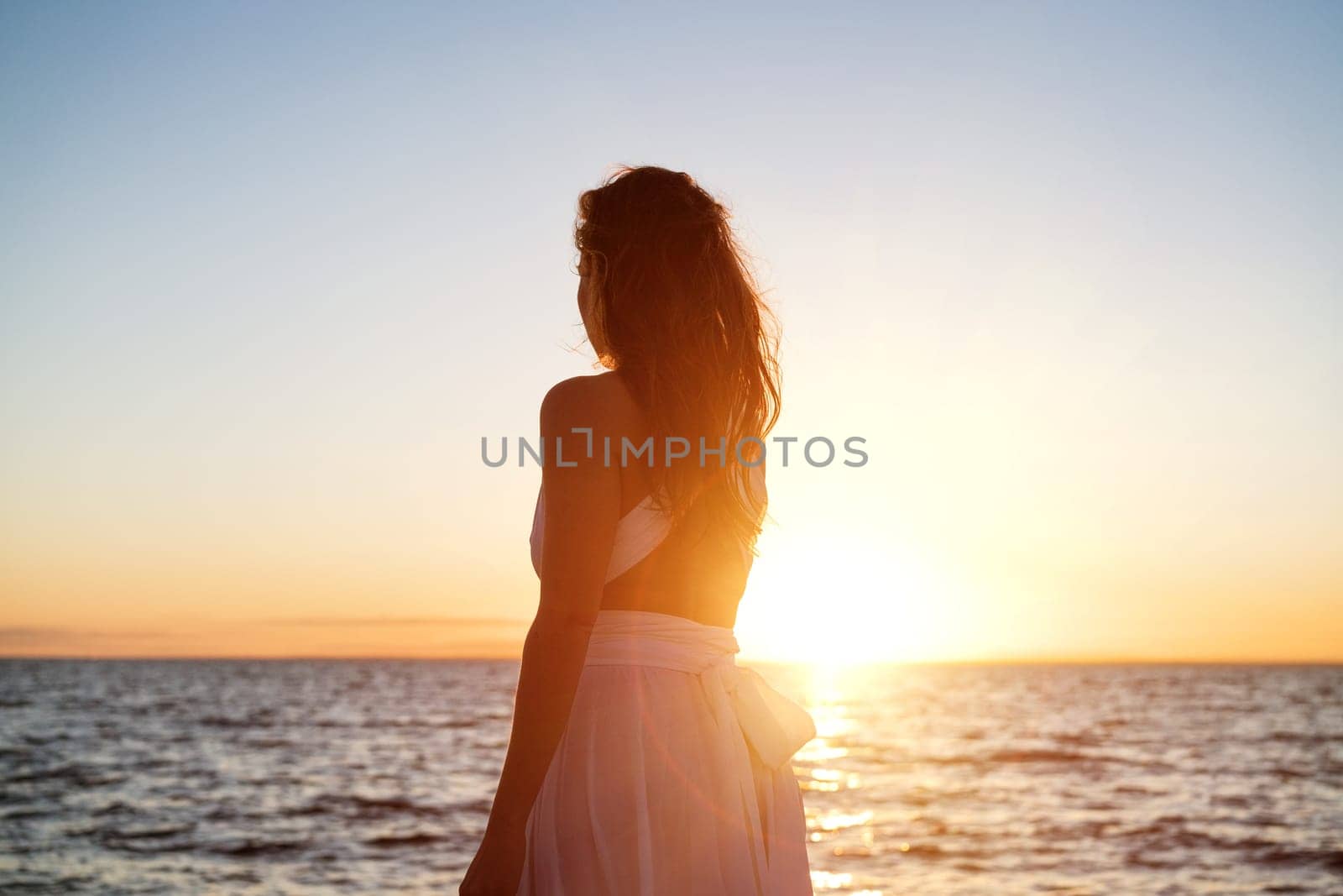 Beautiful woman posing on the beach at sunset in a white dress by EkaterinaPereslavtseva