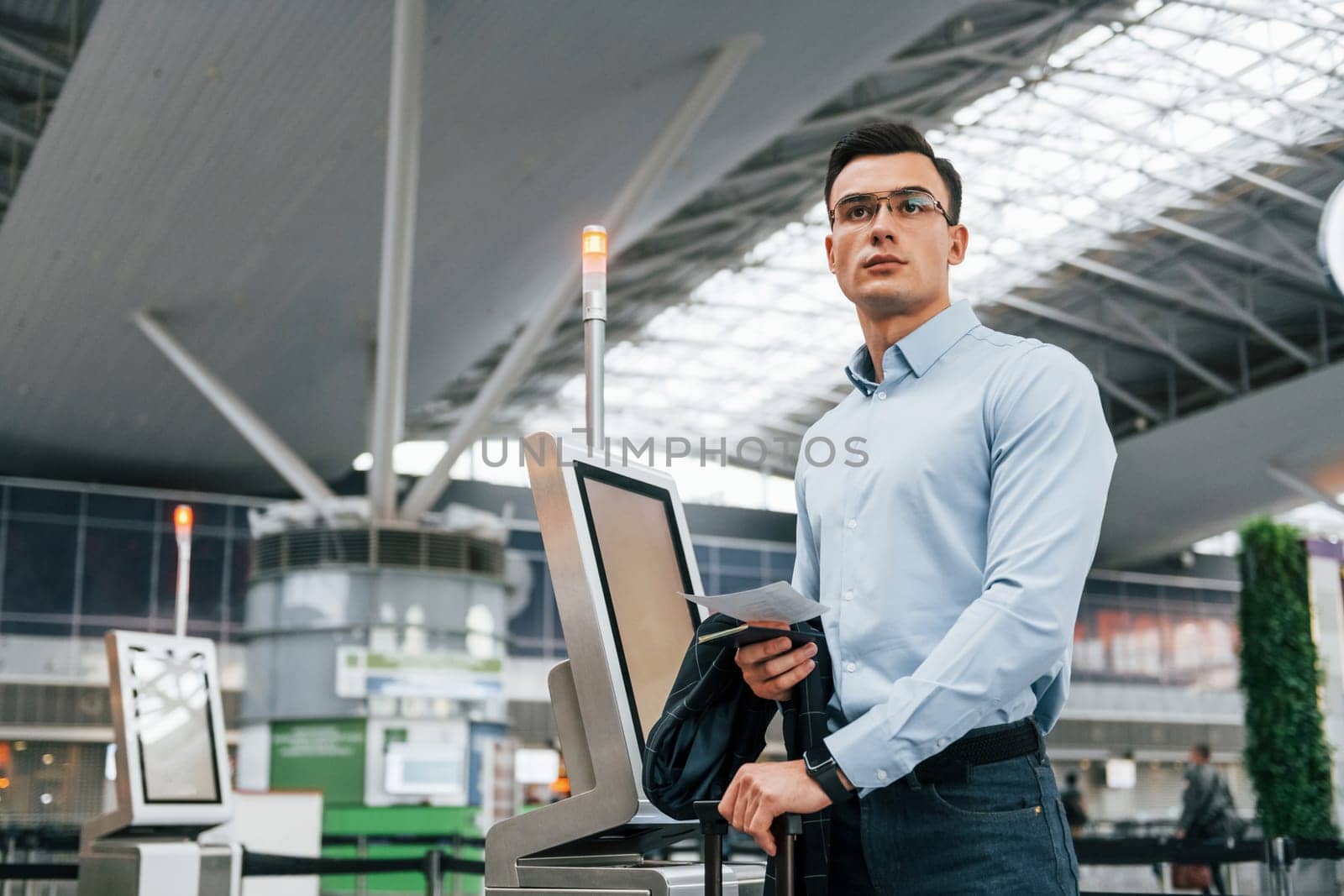 Standing by the terminal. Young businessman in formal clothes is in the airport at daytime.