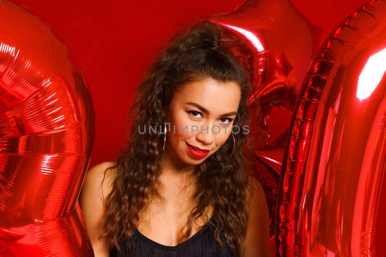 Portrait of happy 30 year old woman on red background with red balloons. A beautiful girl of Caucasian appearance is celebrating her anniversary. Balloons in the form of numbers 30 and stars.